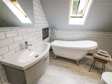 A bathroom with a clawfoot bathtub sink with a mirror and a stool with towels at The Stables in Belbroughton