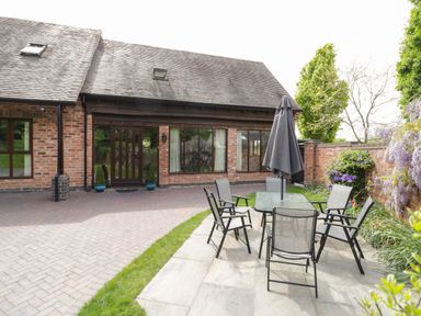 An outdoor patio with a glass table and six chairs under a closed umbrella at The Stables in Belbroughton