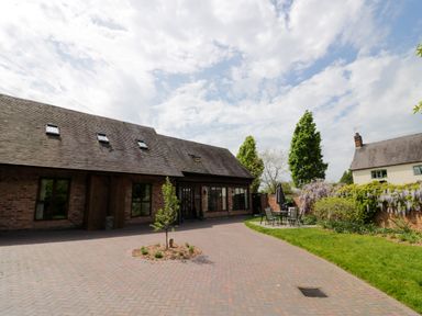 A courtyard with a brick paved area and a small tree in the center surrounded by a lawn and outdoor table set at The Stables in Belbroughton