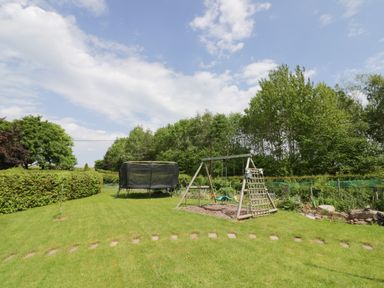 A garden with a trampoline and swing set with greenery and trees at The Stables in Belbroughton