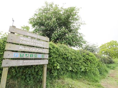 A wooden sign for Waseley Hills Country Park North Car Park with greenery and trees in the background at The Stables in Belbroughton