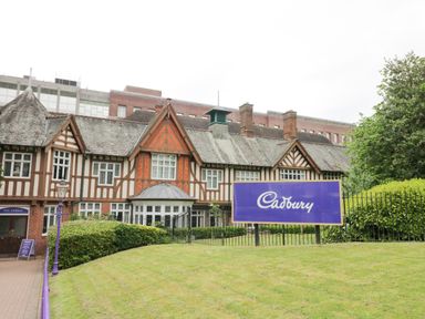 A traditional building with timber framing and a large purple Cadbury sign on a lawn in front of it