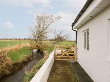 A small wooden gate next to a white building with a stream and wooden footbridge in a rural area at The Annex in Ulverston