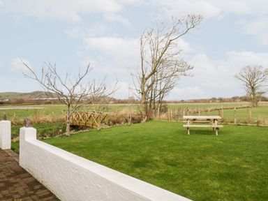 An outdoor garden area with a wooden picnic table a small wooden bridge leafless trees and green grass at The Annex in Ulverston