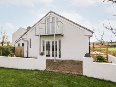 A white house with a glass balcony and patio doors facing a grassy yard at The Annex in Ulverston