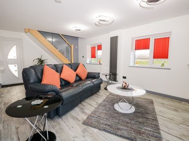 A living room with a black leather sofa and orange cushions with two round tables a rug and red window blinds at The Annex in Ulverston