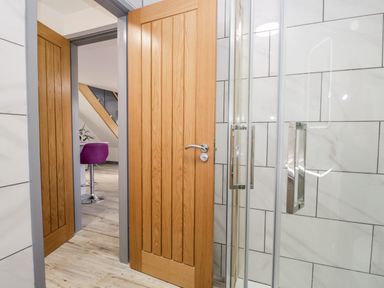 A bathroom with a wooden door and a glass shower enclosure showing a room with a purple chair at The Annex in Ulverston