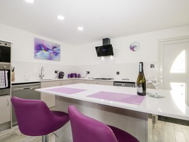 A kitchen with a white island counter purple chairs and purple accents at The Annex in Ulverston