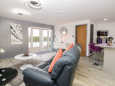 A living room with a black leather sofa and orange pillows next to white round tables and purple bar stools at The Annex in Ulverston