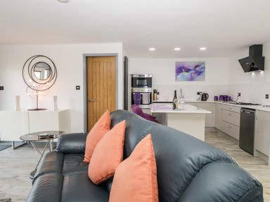 A black leather sofa with orange cushions in an open kitchen and living area with wooden door and modern kitchen appliances at The Annex in Ulverston