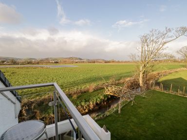 A balcony with a metal table overlooking a grassy field with a wooden bridge and trees at The Annex in Ulverston