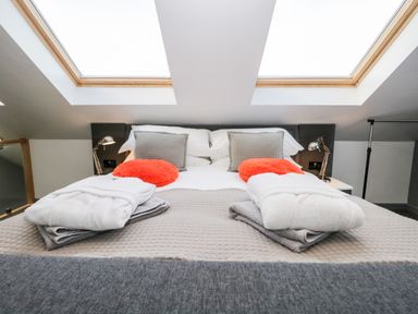 A bedroom with a bed featuring gray and orange pillows white robes and skylights above at The Annex in Ulverston