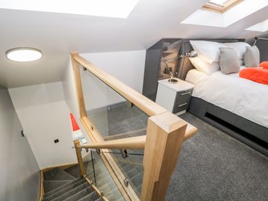 A staircase with wooden handrail and glass panels next to a bedroom with a bed bedside table and lamp at The Annex in Ulverston