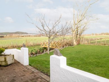 An outdoor garden with a lawn a wooden bridge trees and a white wall at The Annex in Ulverston