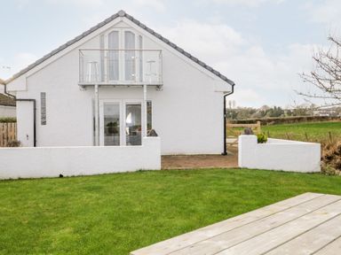 A white house with a small balcony and glass doors overlooking a grassy yard at The Annex in Ulverston