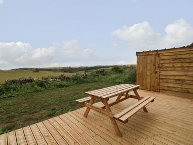 A wooden picnic table on a wooden deck next to a wooden shed with fields and hills in the background at Dew Pond in Blagdon
