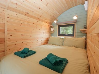 A bedroom with a double bed and folded towels on it inside a wooden cabin at Dew Pond in Blagdon
