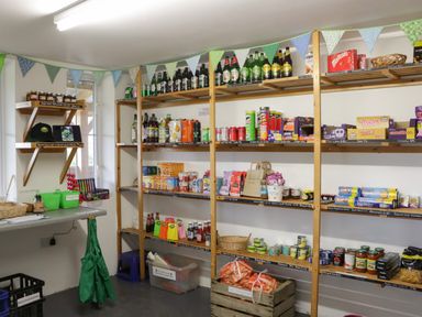 A small shop room with wooden shelves filled with drinks snacks and groceries at Dew Pond in Blagdon