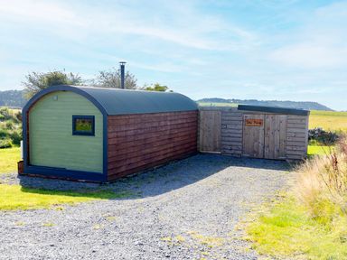 A small wooden cabin with a curved roof and a shed with a sign reading Dew Pond in a rural area at Dew Pond in Blagdon