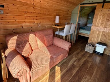 A wooden interior room with a striped sofa two chairs at a small table and a view into a bedroom at Dew Pond in Blagdon