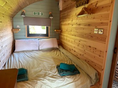 A bedroom with a bed pillows towels window and wooden walls at Dew Pond in Blagdon