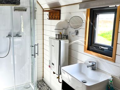 A bathroom with a shower enclosure sink water heater window and wall-mounted mirror at Dew Pond in Blagdon