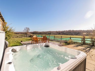An outdoor hot tub and wooden table with chairs on a deck overlooking fields at Thistleyhaugh Cottage in Longhorsley near Longframlington