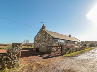 A stone cottage with a wooden gate and surrounding wall on a dirt road at Thistleyhaugh Cottage in Longhorsley near Longframlington
