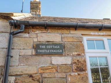 Stone exterior wall with a sign reading The Cottage Thistleyhaugh next to a white window at Thistleyhaugh Cottage in Longhorsley near Longframlington