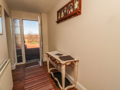 An entrance hallway with a wooden table a striped rug and an open door showing an outdoor area at Thistleyhaugh Cottage in Longhorsley near Longframlington