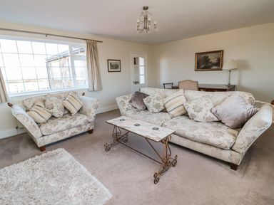 A living room with two floral patterned sofas a metal and wood coffee table a shaggy rug a painting a floor lamp and a large window at Thistleyhaugh Cottage in Longhorsley near Longframlington