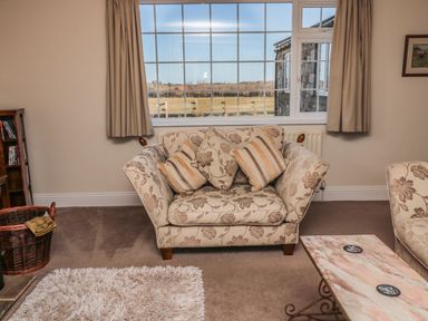 A living room with a floral armchair cushions a window with beige curtains a marble coffee table and a wicker basket at Thistleyhaugh Cottage in Longhorsley near Longframlington