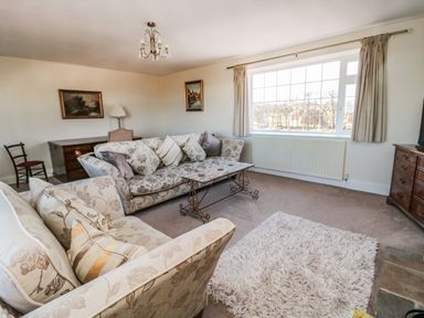 A living room with patterned sofas a coffee table a rug and a large window at Thistleyhaugh Cottage in Longhorsley near Longframlington