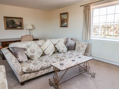 A living room with a floral sofa cushions a marble coffee table paintings a window and a wooden desk at Thistleyhaugh Cottage Longhorsley near Longframlington