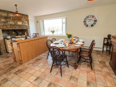 A dining room with a wooden table set for breakfast and wooden chairs near a kitchen area at Thistleyhaugh Cottage Longhorsley near Longframlington