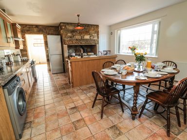A kitchen with a wooden dining table set for breakfast and kitchen appliances at Thistleyhaugh Cottage in Longhorsley near Longframlington