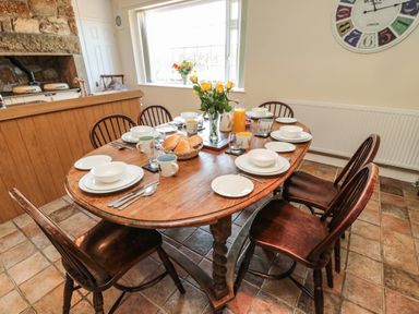 A dining room with a wooden table set for breakfast and six chairs at Thistleyhaugh Cottage Longhorsley near Longframlington
