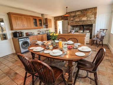 A kitchen with a wooden dining table set for breakfast and wooden chairs at Thistleyhaugh Cottage in Longhorsley near Longframlington