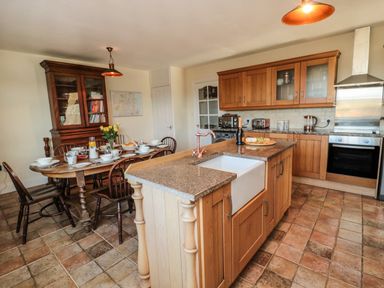 A kitchen with wooden cabinets an island with a sink and a dining table set for a meal at Thistleyhaugh Cottage in Longhorsley near Longframlington