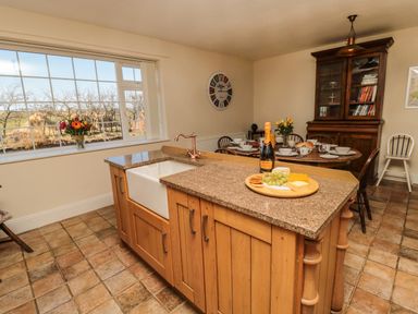 A kitchen with a wooden island and sink and a dining table set with dishes and flowers at Thistleyhaugh Cottage in Longhorsley near Longframlington