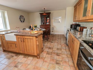 A kitchen with wooden cabinets a dining table with chairs and a china cabinet at Thistleyhaugh Cottage in Longhorsley near Longframlington