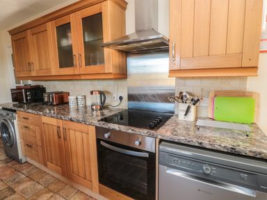 A kitchen with wooden cabinets a countertop with appliances including a toaster kettle and microwave with an oven and dishwasher below at Thistleyhaugh Cottage in Longhorsley near Longframlington