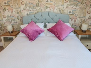 A bed with a tufted headboard two pink pillows and white bedding with two bedside tables and lamps at Thistleyhaugh Cottage in Longhorsley near Longframlington