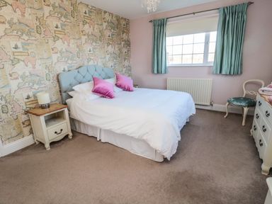 A bedroom with a bed pink pillows nightstand lamp window and chair at Thistleyhaugh Cottage in Longhorsley near Longframlington