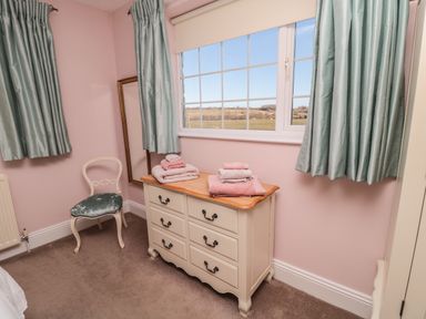 A bedroom corner with a dresser, chair, window with curtains and towels on the dresser at Thistleyhaugh Cottage Longhorsley near Longframlington