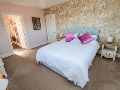 A bedroom with a bed with white bedding and pink pillows bedside tables and a door at Thistleyhaugh Cottage in Longhorsley near Longframlington