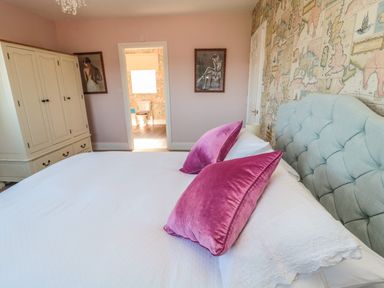 A bedroom with a bed with white bedding and pink pillows a wardrobe and two framed pictures on the walls at Thistleyhaugh Cottage in Longhorsley near Longframlington