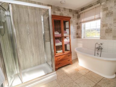 A bathroom with a glass shower enclosure a wooden cabinet with towels and a freestanding bathtub near a window at Thistleyhaugh Cottage in Longhorsley near Longframlington