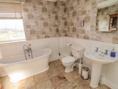 A bathroom with a bathtub toilet sink and a mirror with newspaper print wallpaper at Thistleyhaugh Cottage in Longhorsley near Longframlington