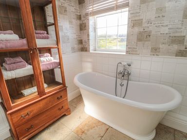 A bathroom with a freestanding bathtub and a wooden cabinet with towels at Thistleyhaugh Cottage in Longhorsley near Longframlington